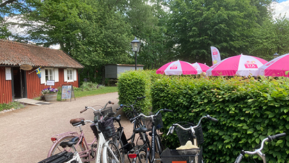 En röd stuga, gröna träd, parasoll och cyklar